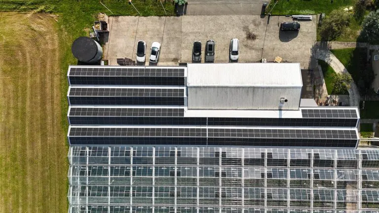 Luchtfoto van een bedrijfsdak vol zonnepanelen naast de kassen
